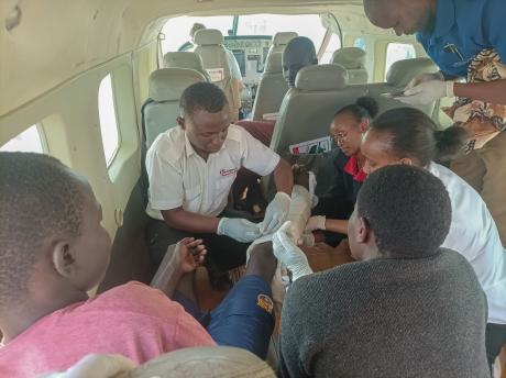 The E plus team administers first aid to a patient inside the aircraft, securing wooden splints on his fractured leg to minimize movement during the transfer.